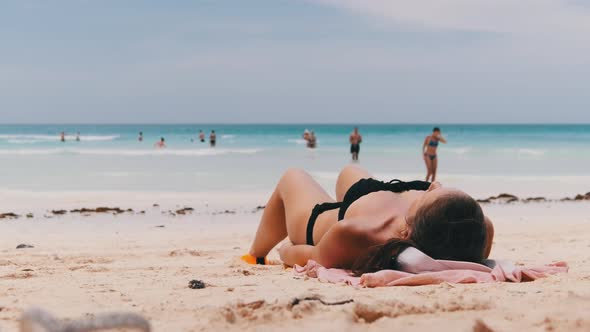 Young Woman Sunbathes on a Paradise Sandy Beach Lying in Black Bikini Near Ocean alt