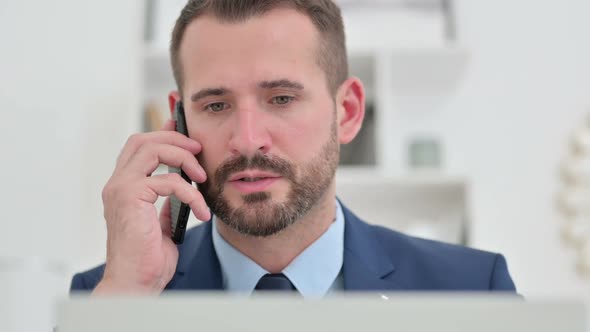 Portrait of Businessman with Laptop Talking on Smartphone alt