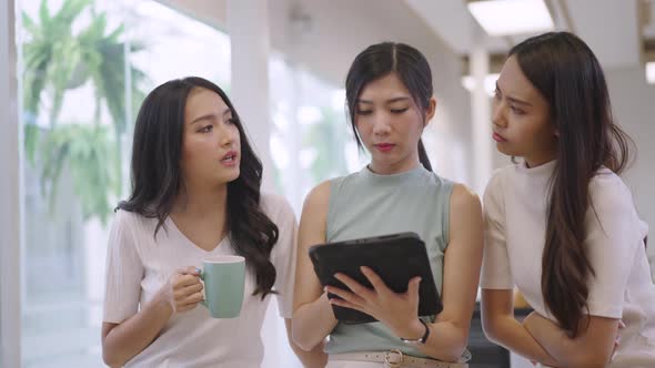 Asian female colleagues looking at tablets together in the office with seriousness