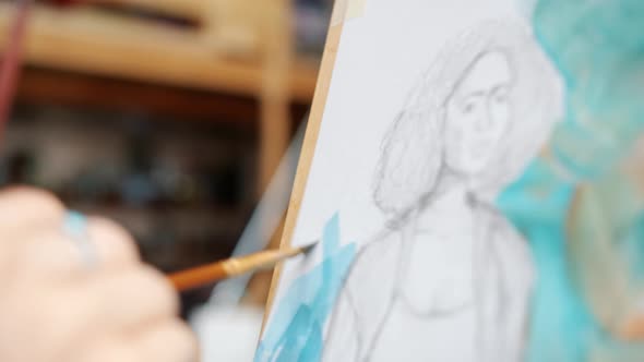 Close-up of Girl's Hand Painting Portrait of Woman with Watercolors in Studio alt