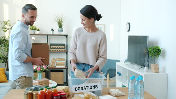Beautiful Couple Packing Groceries for Donation and Talking Indoors at Home alt