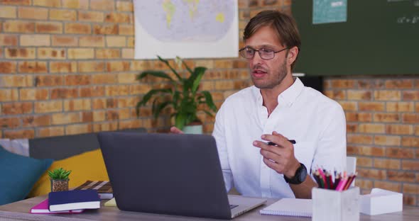Caucasian male teacher teaching on videocall on laptop in the classroom at school alt
