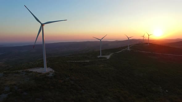 Sun setting behind elegant windmills on a hill alt