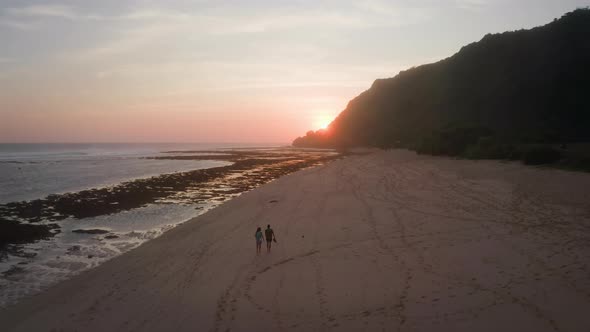 A Couple Walking Along Sandy Beach at Sunset