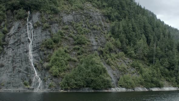 Small waterfalls run down a mountain into the ocean water of an Alaskan fjord. The camera moves para alt