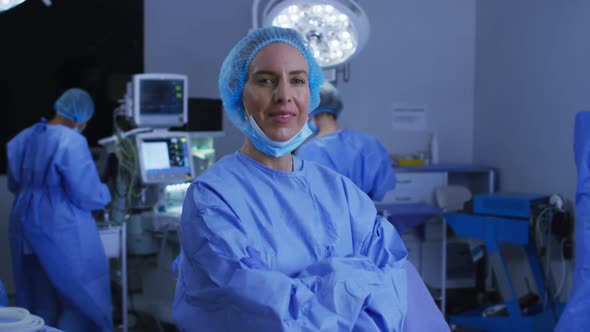 Portrait of caucasian female surgeon in lowered face mask smiling to camera in operating theatre alt