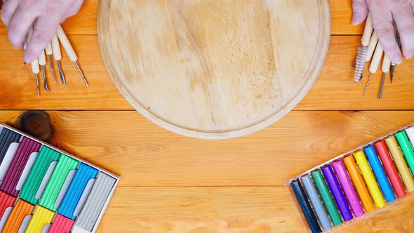 The artist lays lays out plasticine modelling tools kit on a wooden desk in the classroom studio