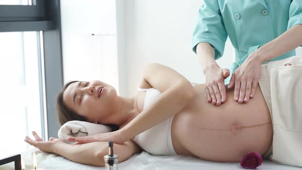 Professional Massage Therapist Massages Arm and Shoulders of Young Pregnant Woman
