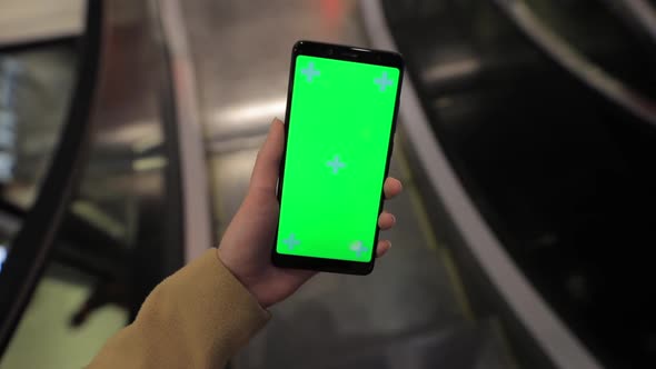 POV Female Hand Holding Smartphone Green Screen in a Mall Escalator