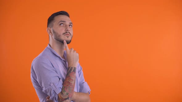 Thoughtful Man Thinking with Finger on Face, Isolated on Orange Background. alt