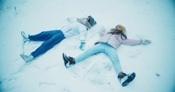 Young Woman and Daughter Lie on Ground Making Snow Angels alt