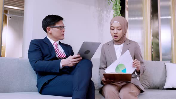 Two male and female hijab business colleagues using digital tablet, notepad and discussing project alt