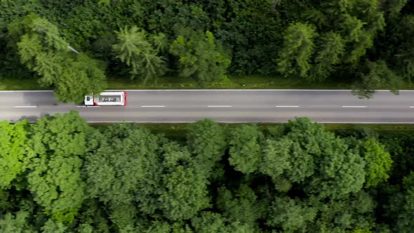 Tracking a big lorry driving through a straight street in a forest, aerial following shot by a drone alt