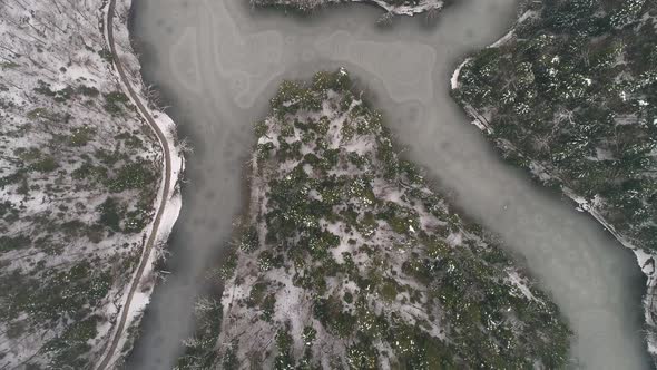 Aerial shot of frozen lake surrounded by forest at winter alt