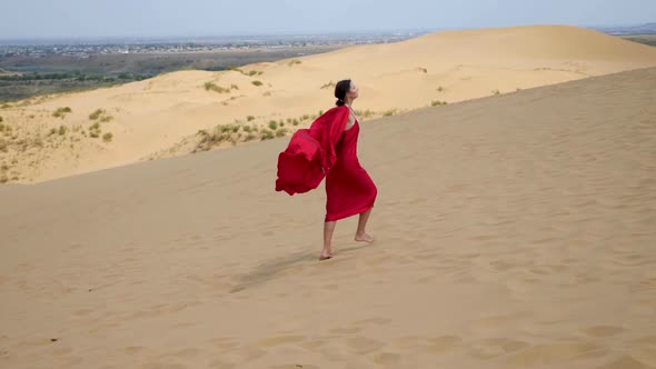 Sexy Brunette Woman in a Red Satin Long Dress Walks on Sand Dunes in the Desert alt