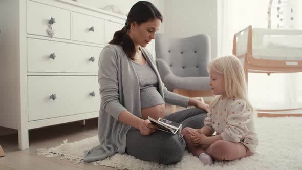 Caucasian woman in advanced pregnancy browsing ultrasound scan with her elementary daughter. alt