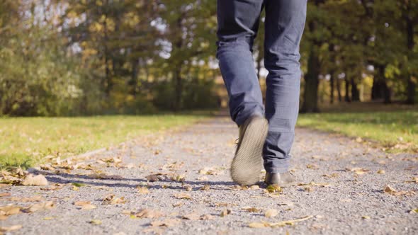 A Man Walks Down a Leafcovered Pathway Through a Park in Fall  Closeup on the Legs