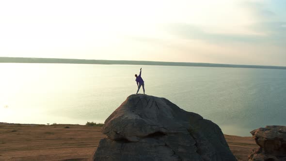 A Girl is Doing Fitness on a Hill on the Lake Shore