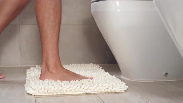 Man Sitting on Wc Toilet Bowl at the Bathroom and Holding a Toilet Paper Roll alt