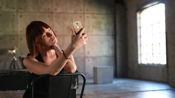 young beautiful woman indoor sitting chair using smart phone taking selfie alt