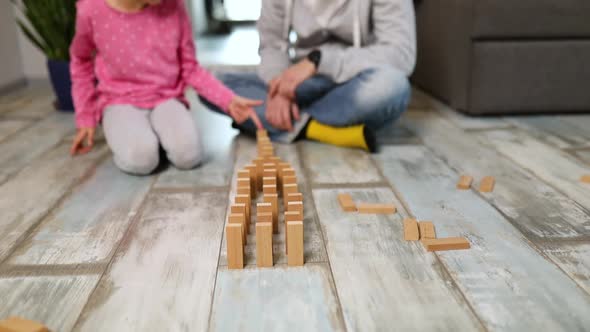 Father and happy daughter play wooden blocks domino falling down alt