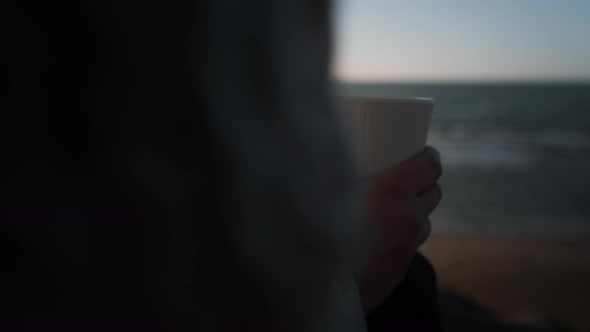 Woman Holding Steaming Coffee Cup On Sunlit Beach alt
