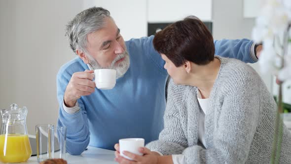 Portrait of Relaxed Positive Senior Bearded Man Drinking Morning Coffee Talking with Wife in Kitchen alt