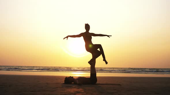 Fit Sporty Couple Practicing Acro Yoga with Partner Together on the Sandy Beach