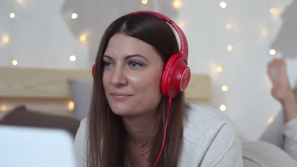 A Beautiful Girl is Lying on the Bed Using a Mobile Computer of White Color and Listening to Music alt