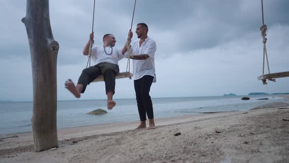 Married Happy Gay Couple Having Fun on a Beach Seaside Swing alt