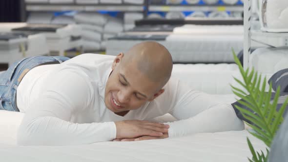 Young Man Trying Orthopedic Mattress at Furniture Store