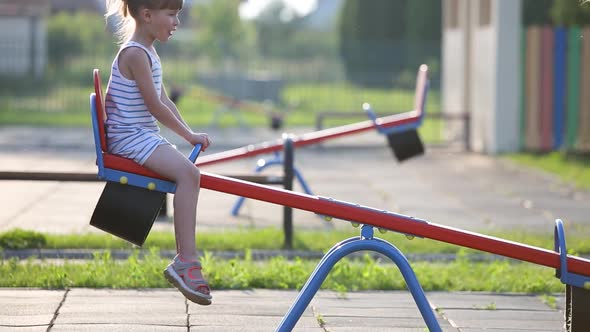 Cute Child Girl Playing Outside on a Seesaw Swing at Preschool Playground alt