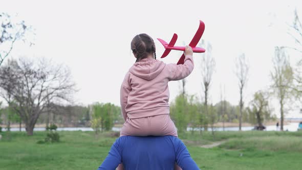 Happy family, dad, little daughter play together with a toy plane in the park. alt