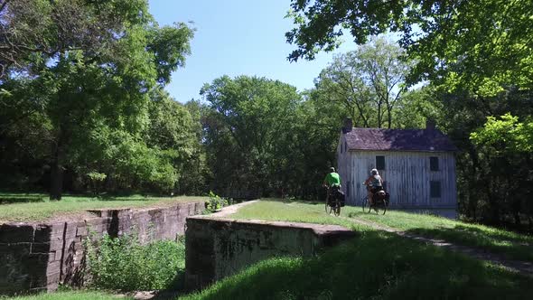 Bicycle tourists on the C&O canal in Maryland along the Potomac River going by a lock house along th alt