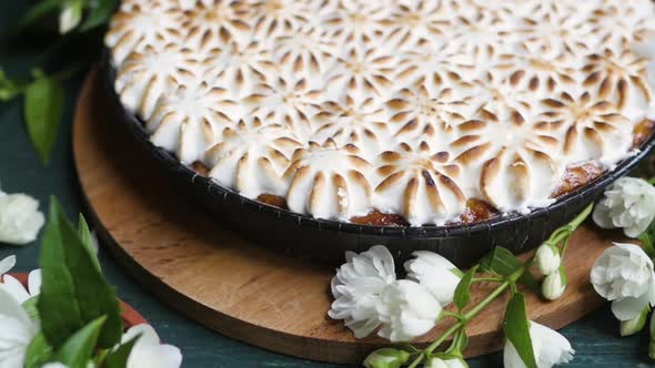 Beautiful Pie with White Meringue Cream on a Wooden Background Among White Flowers. Viewpoint From alt