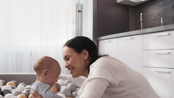 Loving Asian Mother Cuddling Baby in Ball Pool alt