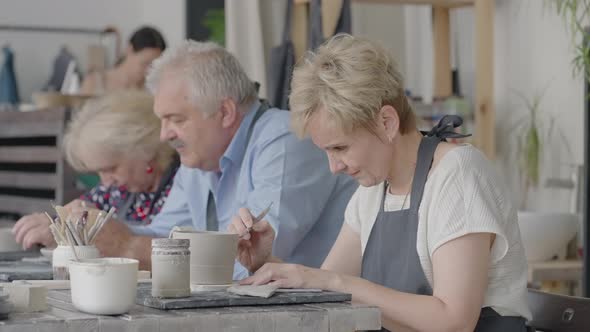 A Group of Elderly People at a Master Class in Pottery Together Sculpt and Cut a Drawing on Cups of alt