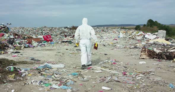 Ecologist in Protective Suit and Mask Walking with Tablet Among Polluted Land alt