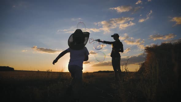 Young Mom and Little Son in the Sunset Catches Soap Bubbles in Meadow. Relax with Child in Nature alt