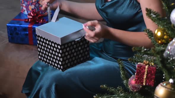 Young Woman Opens a Gift Box with Medical Masks Inside While Sitting Near a Christmas Tree