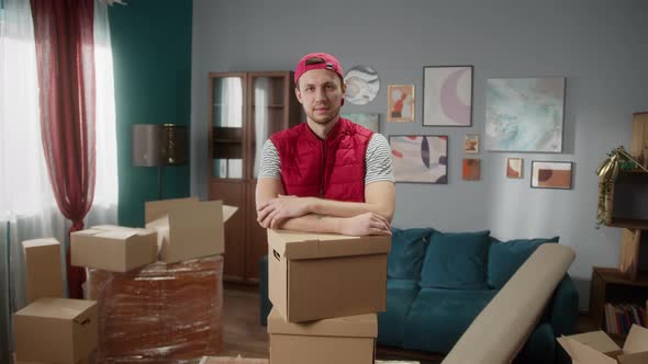 Delivery Man Holding Boxes in New Apartment and Crossing Hands alt