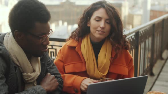 Multiethnic Colleagues Using Laptop and Talking in Rooftop Cafe alt