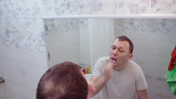 A man plucks hair from his nose, stands in the bathroom in front of a mirror alt