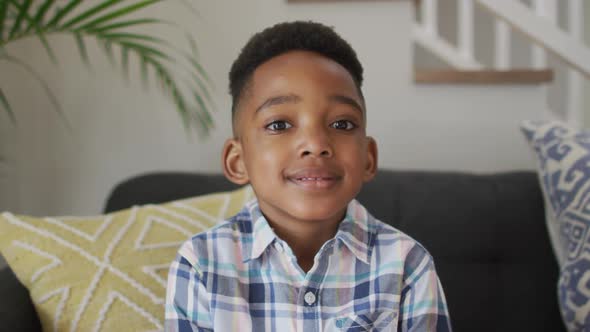 African american boy siting on sofa, looking at camera and smiling alt