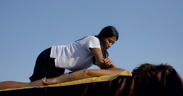 Close-up Massage on the Seashore on a Special Table. Asian Masseuse Massages the Back and Shoulder alt