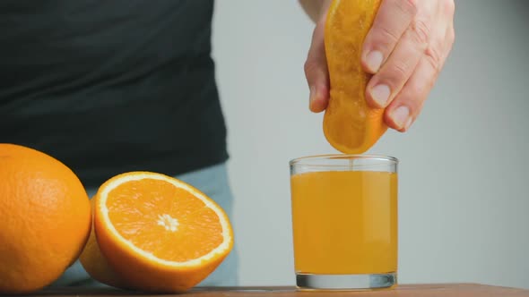 Male hand squeezing out fresh juice from orange citrus fruit into glass in the home kitchen