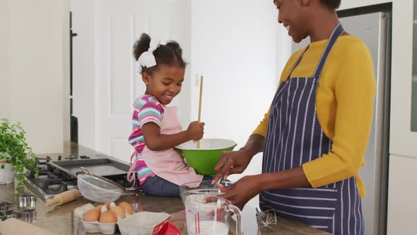 Happy african american mother and daughter wearing aprons cooking in kitchen alt