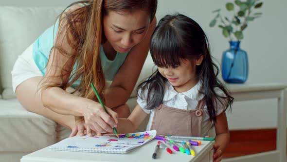 Young mother teaching little daughter drawing on paper