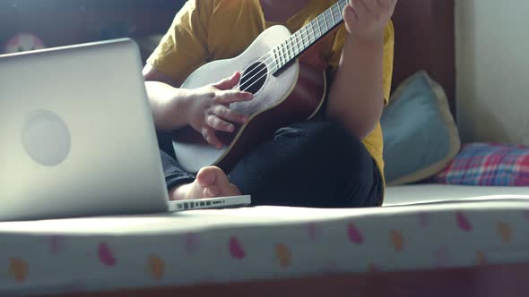 Little asian boy musician playing ukulele at home alt
