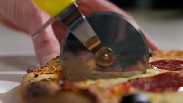 baker cuts fresh hot pizza with cheese slices of pepperoni with a round knife